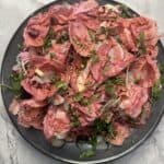 Vibrant pink radicchio salad with microgreens, thinly sliced radishes, shaved parmesan, and a drizzle of tangy vinaigrette, served on a black plate. This colorful dish is a perfect blend of crisp textures and bold flavors, making it a visually striking and delicious salad option for any occasion.