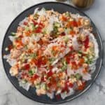 Spicy salmon crispy rice chips topped with tobiko, diced cucumber, green onions, and black sesame seeds on a black plate. A gourmet fusion appetizer or snack featuring crunchy rice crackers, creamy spicy salmon, and vibrant garnishes, perfect for seafood lovers.