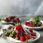 Plates of vibrant beet salad with crumbled cheese, thinly sliced red onions, fresh parsley, and walnuts on a light textured background. The salad is artfully arranged, highlighting the contrast of colors and textures.