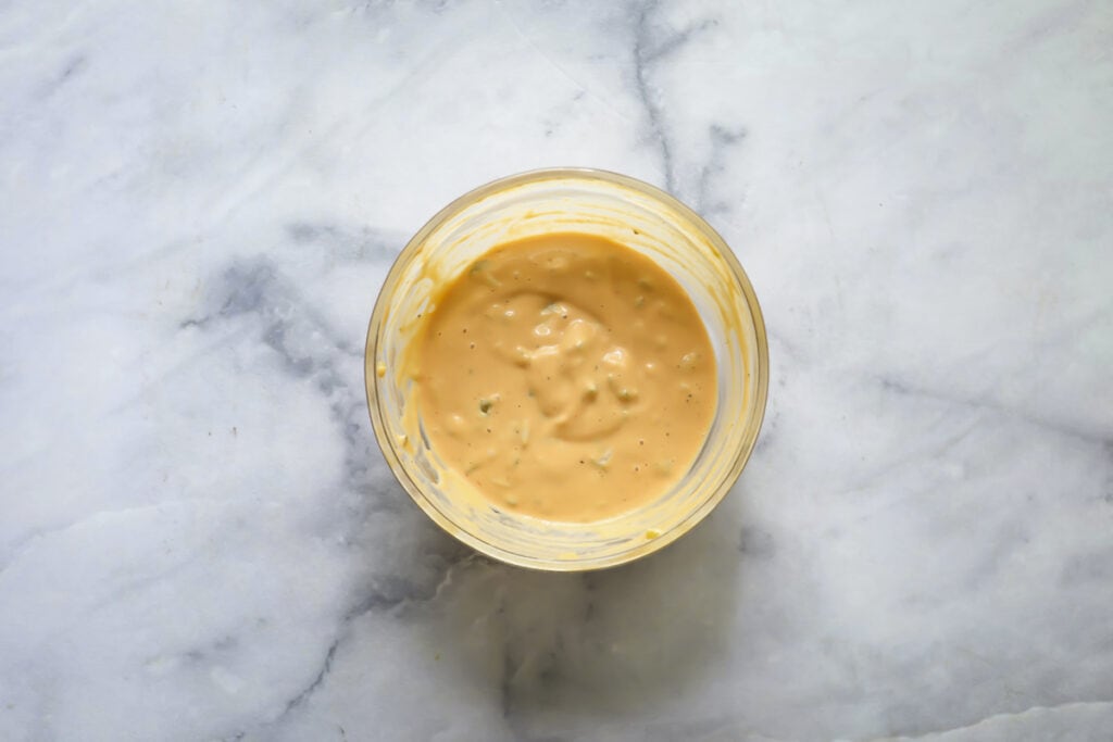 A small glass bowl filled with creamy, orange-colored sauce sits on a light gray marble surface.