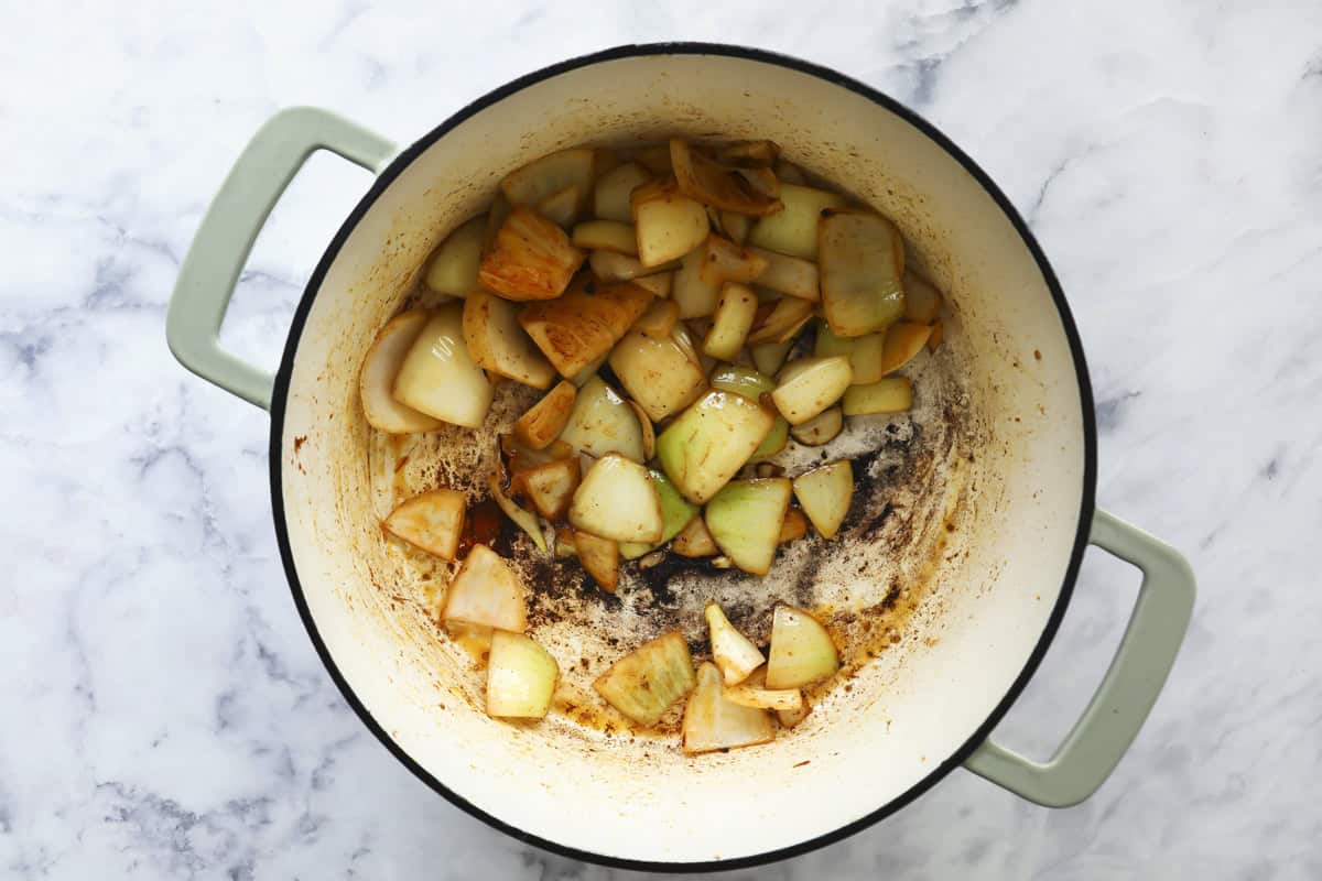 Diced onions being sautéed and browned in a large light green pot on a marble countertop, with some caramelization visible at the bottom of the pot.