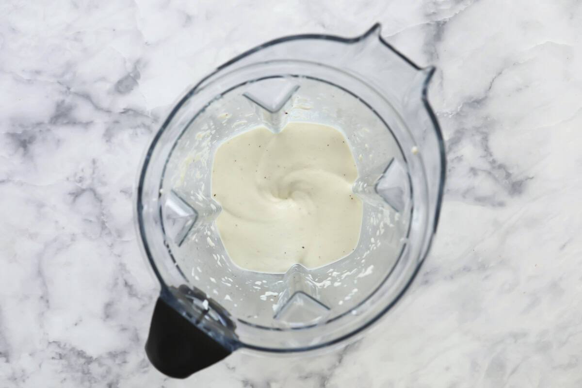 Top view of a blender containing a thick, creamy white mixture, set on a light gray marble surface. The blender is partially filled, and the mixture appears to be smoothly blended.