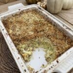 A baked Potato Gattò casserole with a golden, crispy breadcrumb topping in a white rectangular dish, partially served. Decorative pumpkins are on the wooden table in the background.