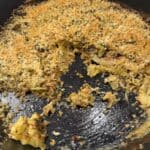 A black cast iron skillet with a golden-brown breadcrumb-topped cabbage gratin, partially served to reveal the crispy topping and tender cabbage gratin layers beneath.