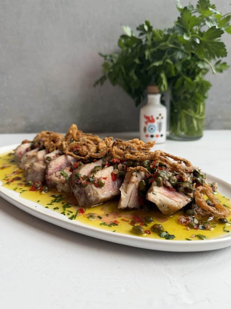 Sliced seared tuna topped with crispy fried onions and herbs, served on a platter with a bright yellow sauce—this 20 Minute Tuna Steak Dinner is garnished with fresh parsley, with a decorative bottle in the background.