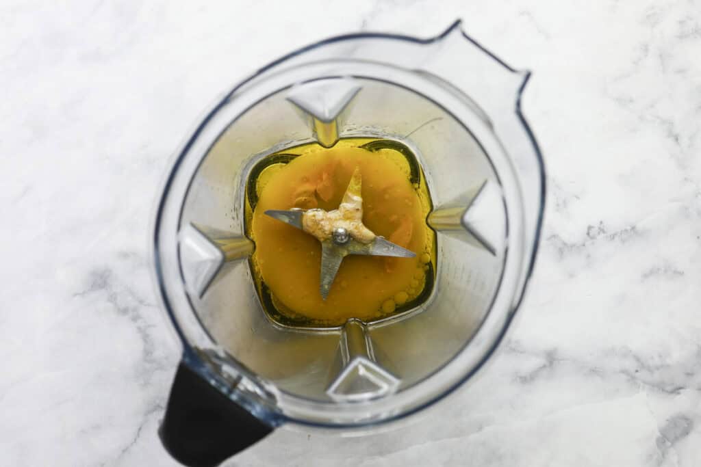 Top view of a blender containing egg yolks and oil on a white marble surface, ready to be mixed for a fresh celery salad dressing.