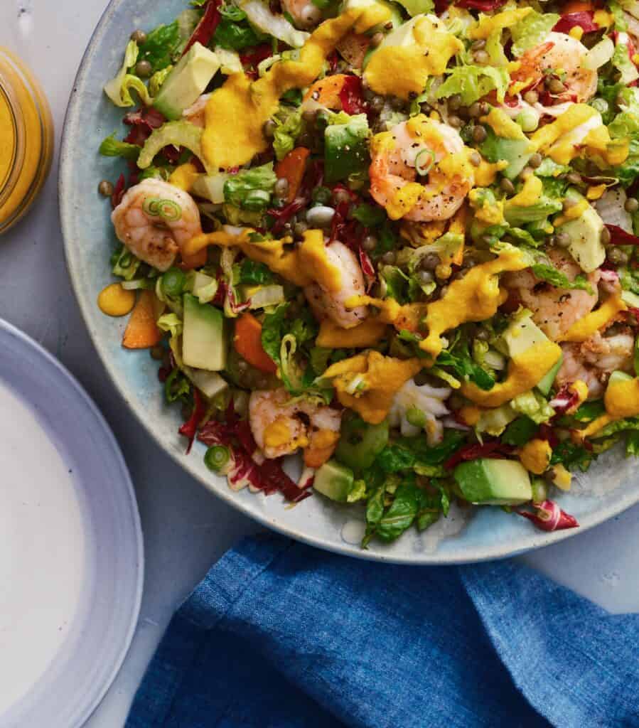 Shrimp and lentil salad with vegetables and carrot dressing on a blue platter.