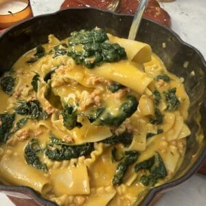 A spoonful of creamy 30 minute savory pumpkin lasagna soup with sausage and kale being lifted from a large pan.