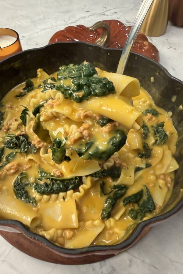 A spoonful of creamy 30 minute savory pumpkin lasagna soup with sausage and kale being lifted from a large pan.