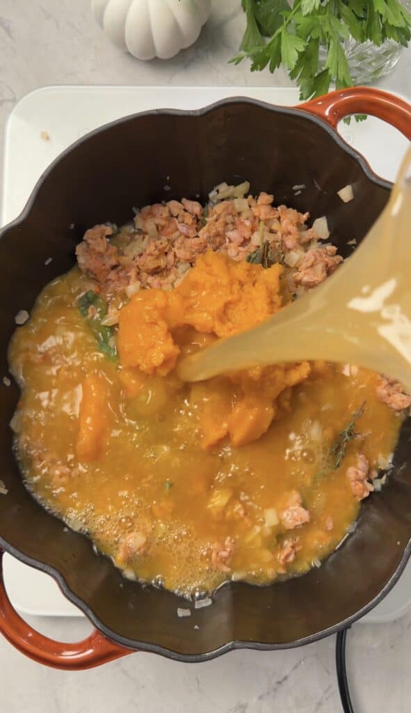 Broth is poured into an orange pot to prepare savory pumpkin lasagna soup, combining cooked ground meat, diced onions, and pumpkin puree.